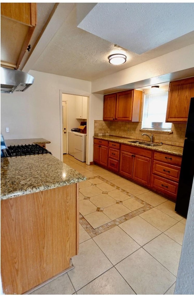 kitchen featuring sink, light stone counters, washer and dryer, decorative backsplash, and exhaust hood