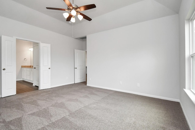 unfurnished bedroom with dark colored carpet, ensuite bathroom, and ceiling fan