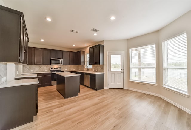 kitchen featuring a center island, light hardwood / wood-style flooring, decorative backsplash, dark brown cabinets, and stainless steel appliances