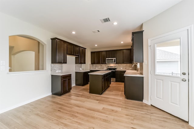 kitchen with dark brown cabinetry, stainless steel appliances, light hardwood / wood-style flooring, backsplash, and a kitchen island