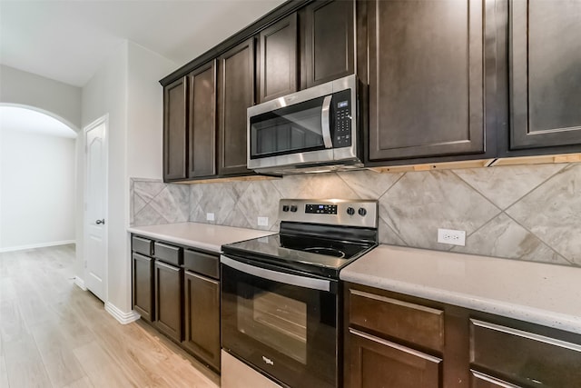 kitchen with dark brown cabinets, light wood-type flooring, stainless steel appliances, and tasteful backsplash