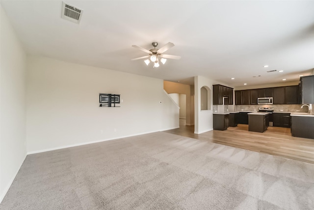 unfurnished living room with ceiling fan, sink, and light carpet