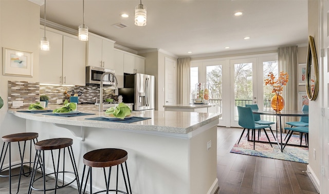 kitchen with white cabinets, appliances with stainless steel finishes, decorative light fixtures, and a kitchen breakfast bar