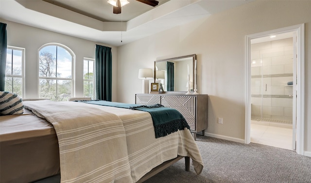 carpeted bedroom with ensuite bathroom, ceiling fan, and a tray ceiling