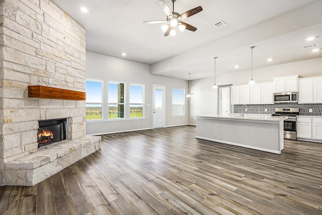 kitchen with dark hardwood / wood-style floors, an island with sink, decorative backsplash, white cabinets, and appliances with stainless steel finishes