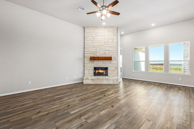 unfurnished living room featuring dark hardwood / wood-style floors, ceiling fan, and a stone fireplace