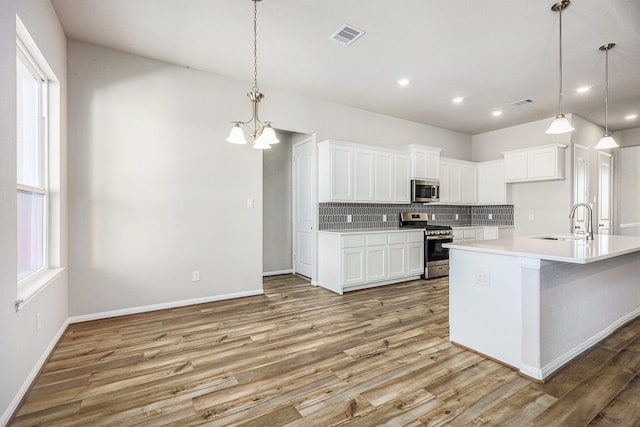 kitchen with appliances with stainless steel finishes, sink, hardwood / wood-style flooring, white cabinets, and an island with sink