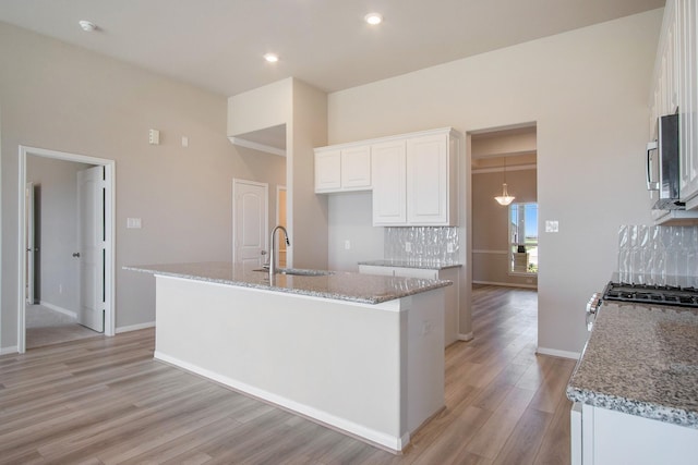 kitchen with white cabinets, a center island with sink, sink, light hardwood / wood-style flooring, and light stone counters