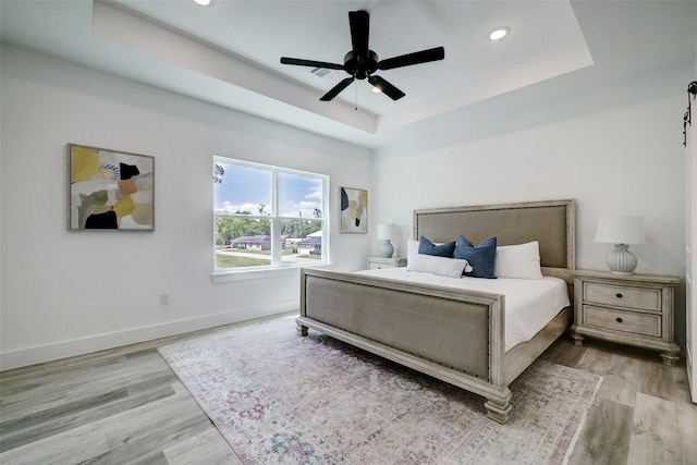 bedroom with a raised ceiling, ceiling fan, and light wood-type flooring