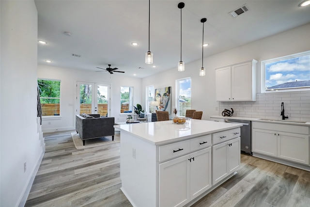 kitchen featuring dishwasher, pendant lighting, a kitchen island, sink, and white cabinetry