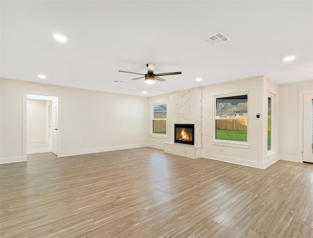 unfurnished living room with ceiling fan, a premium fireplace, and light hardwood / wood-style flooring