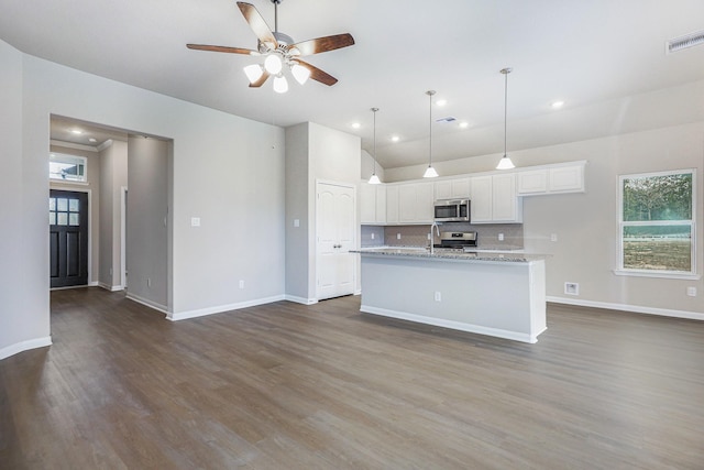 kitchen featuring white cabinets, dark hardwood / wood-style floors, light stone countertops, an island with sink, and stainless steel appliances