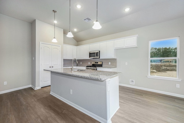 kitchen with lofted ceiling, white cabinets, an island with sink, light stone counters, and stainless steel appliances