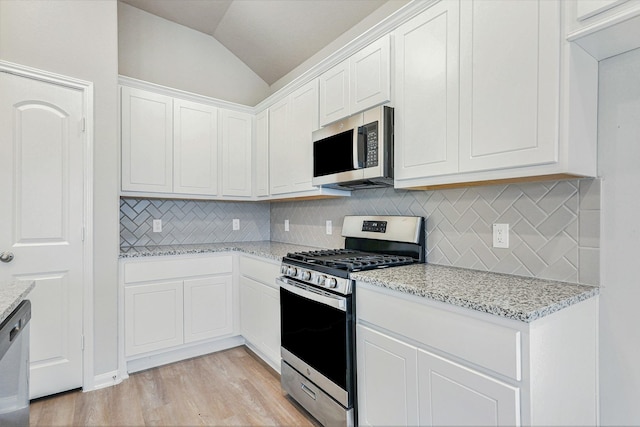 kitchen featuring white cabinetry, stainless steel appliances, tasteful backsplash, light stone counters, and lofted ceiling