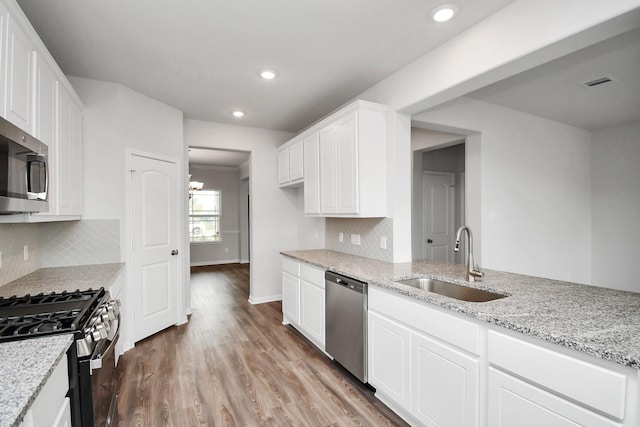 kitchen with white cabinetry, sink, light stone countertops, wood-type flooring, and appliances with stainless steel finishes