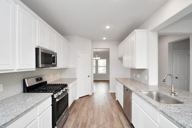 kitchen featuring light stone countertops, appliances with stainless steel finishes, sink, light hardwood / wood-style floors, and white cabinetry