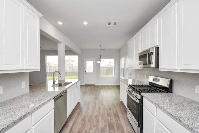 kitchen featuring sink, stainless steel appliances, backsplash, white cabinets, and light wood-type flooring