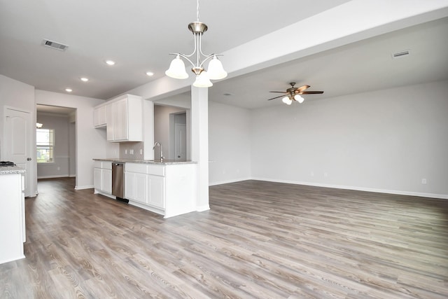 kitchen with light stone counters, ceiling fan with notable chandelier, sink, white cabinets, and light hardwood / wood-style floors