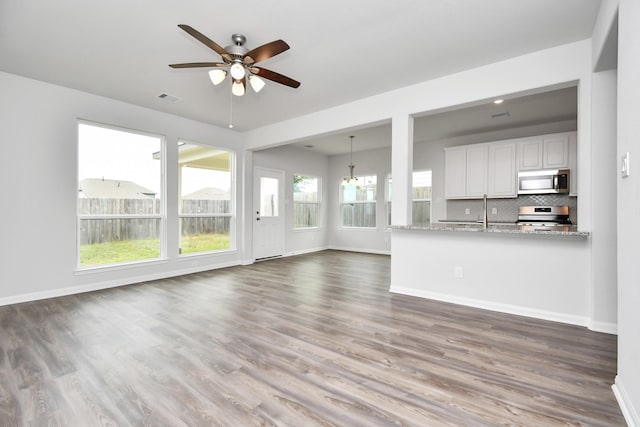 unfurnished living room with ceiling fan with notable chandelier, dark hardwood / wood-style flooring, plenty of natural light, and sink