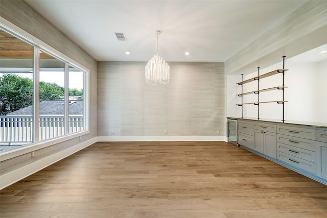 unfurnished dining area featuring light hardwood / wood-style floors, wine cooler, and a chandelier