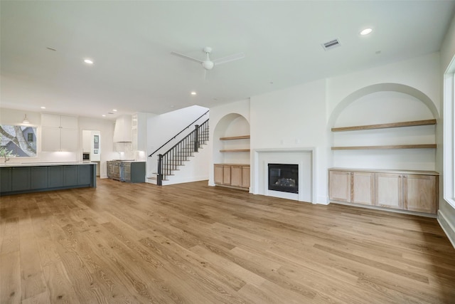 unfurnished living room featuring built in shelves, light hardwood / wood-style floors, and ceiling fan