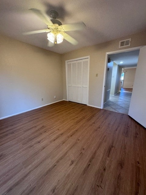 unfurnished bedroom featuring ceiling fan, a closet, dark wood-type flooring, and a textured ceiling