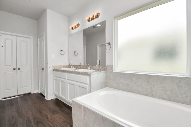 bathroom featuring wood-type flooring, vanity, tiled bath, and plenty of natural light