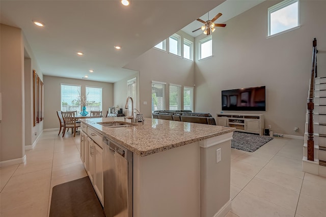 kitchen with a wealth of natural light, a kitchen island with sink, dishwasher, and light stone counters