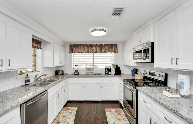 kitchen with light stone countertops, white cabinetry, sink, dark wood-type flooring, and appliances with stainless steel finishes