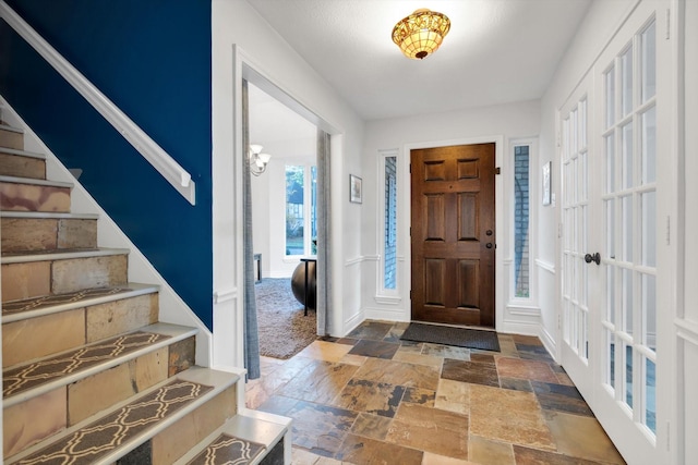 foyer entrance featuring stairs, stone tile flooring, and baseboards