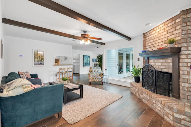 living room featuring baseboards, a ceiling fan, wood finished floors, a brick fireplace, and beam ceiling