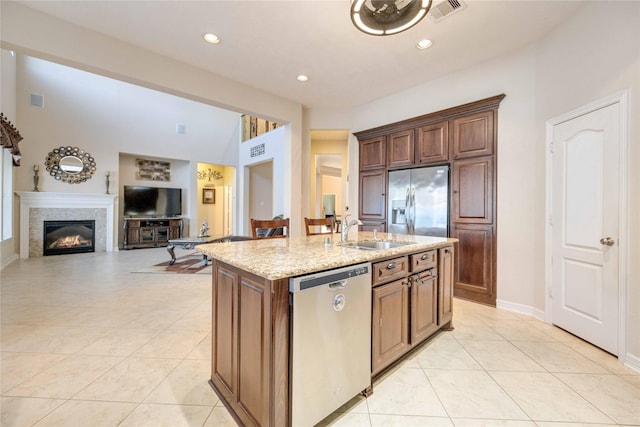 kitchen featuring light stone countertops, sink, a center island with sink, light tile patterned floors, and appliances with stainless steel finishes