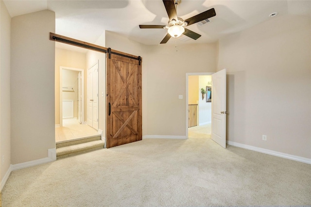 unfurnished bedroom with ceiling fan, a barn door, ensuite bathroom, vaulted ceiling, and light carpet