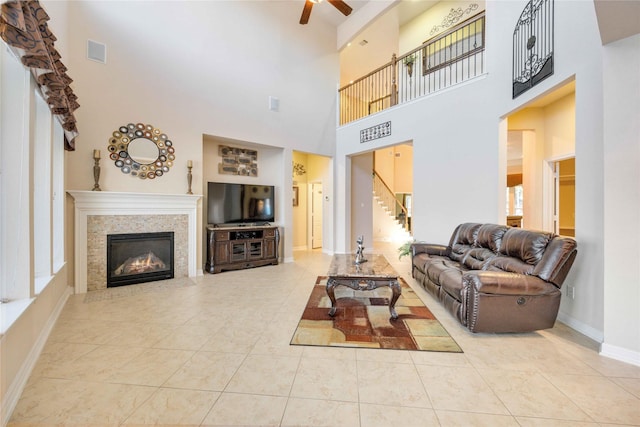 tiled living room with a tile fireplace, a high ceiling, and ceiling fan