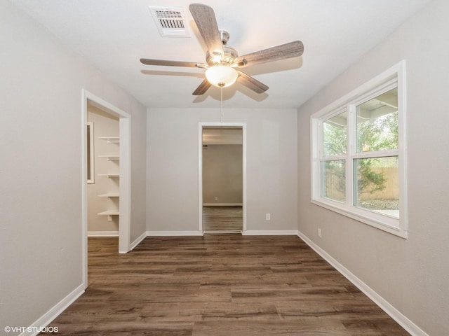 unfurnished bedroom with ceiling fan, dark hardwood / wood-style flooring, a walk in closet, and a closet