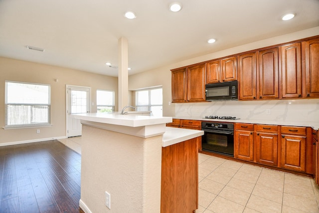 kitchen with light wood-type flooring, an island with sink, tasteful backsplash, and black appliances