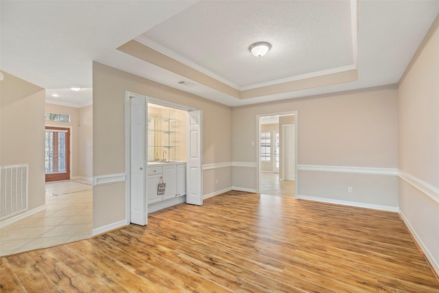 spare room featuring a raised ceiling, crown molding, a textured ceiling, and light wood-type flooring