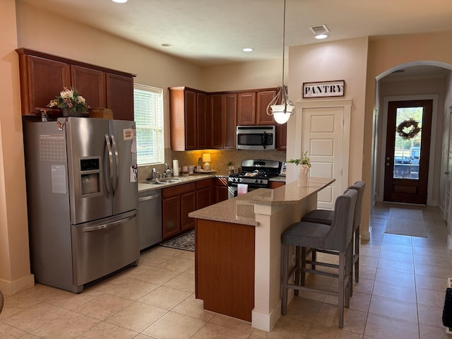 kitchen featuring a breakfast bar area, tasteful backsplash, decorative light fixtures, light stone counters, and stainless steel appliances