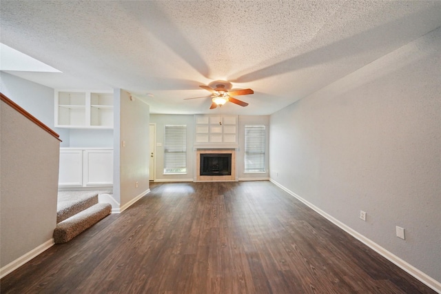 unfurnished living room featuring a textured ceiling, built in shelves, ceiling fan, and dark wood-type flooring