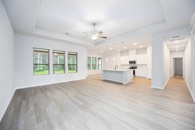 unfurnished living room featuring ceiling fan, light hardwood / wood-style floors, sink, and a tray ceiling