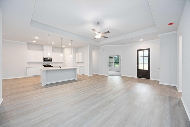 unfurnished living room with a tray ceiling, ceiling fan, crown molding, and light wood-type flooring