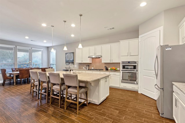 kitchen with decorative light fixtures, dark hardwood / wood-style flooring, a kitchen island with sink, and appliances with stainless steel finishes