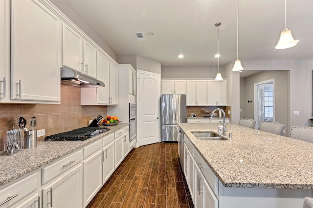 kitchen with stainless steel appliances, sink, white cabinets, dark hardwood / wood-style floors, and an island with sink