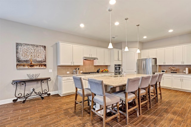 kitchen with pendant lighting, dark hardwood / wood-style floors, stainless steel appliances, and an island with sink