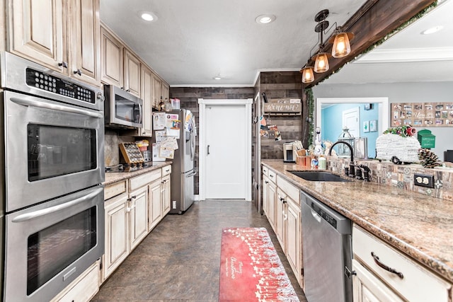 kitchen with cream cabinets, sink, light stone countertops, decorative light fixtures, and stainless steel appliances