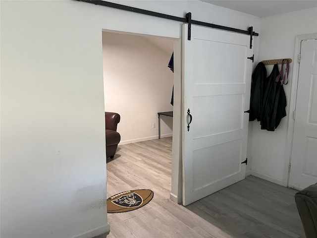 corridor featuring a barn door, wood finished floors, and baseboards