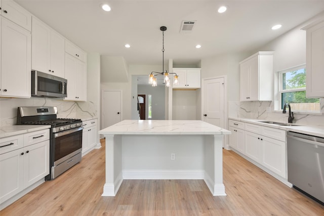 kitchen featuring stainless steel appliances, a kitchen island, a sink, white cabinets, and decorative light fixtures