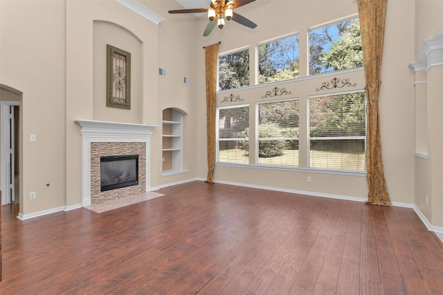 unfurnished living room with a healthy amount of sunlight, dark hardwood / wood-style flooring, a towering ceiling, and built in features