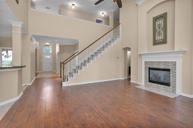 unfurnished living room featuring ceiling fan, a towering ceiling, hardwood / wood-style flooring, a fireplace, and ornamental molding