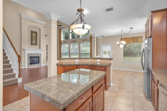 kitchen featuring hanging light fixtures, stainless steel appliances, a stone fireplace, a kitchen island, and light wood-type flooring